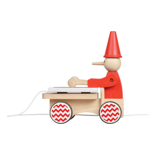 A wooden pull-along toy featuring a character resembling Pinocchio with a red hat, red jacket,  attached to a small wooden xylophone on wheels with a red and white zig-zag pattern.