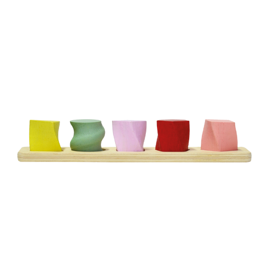 A set of colorful geometric shape sorters on a wooden board. The sorters are in shapes of a sphere, cube, cylinder, cone, and rectangular prism, each a different color.